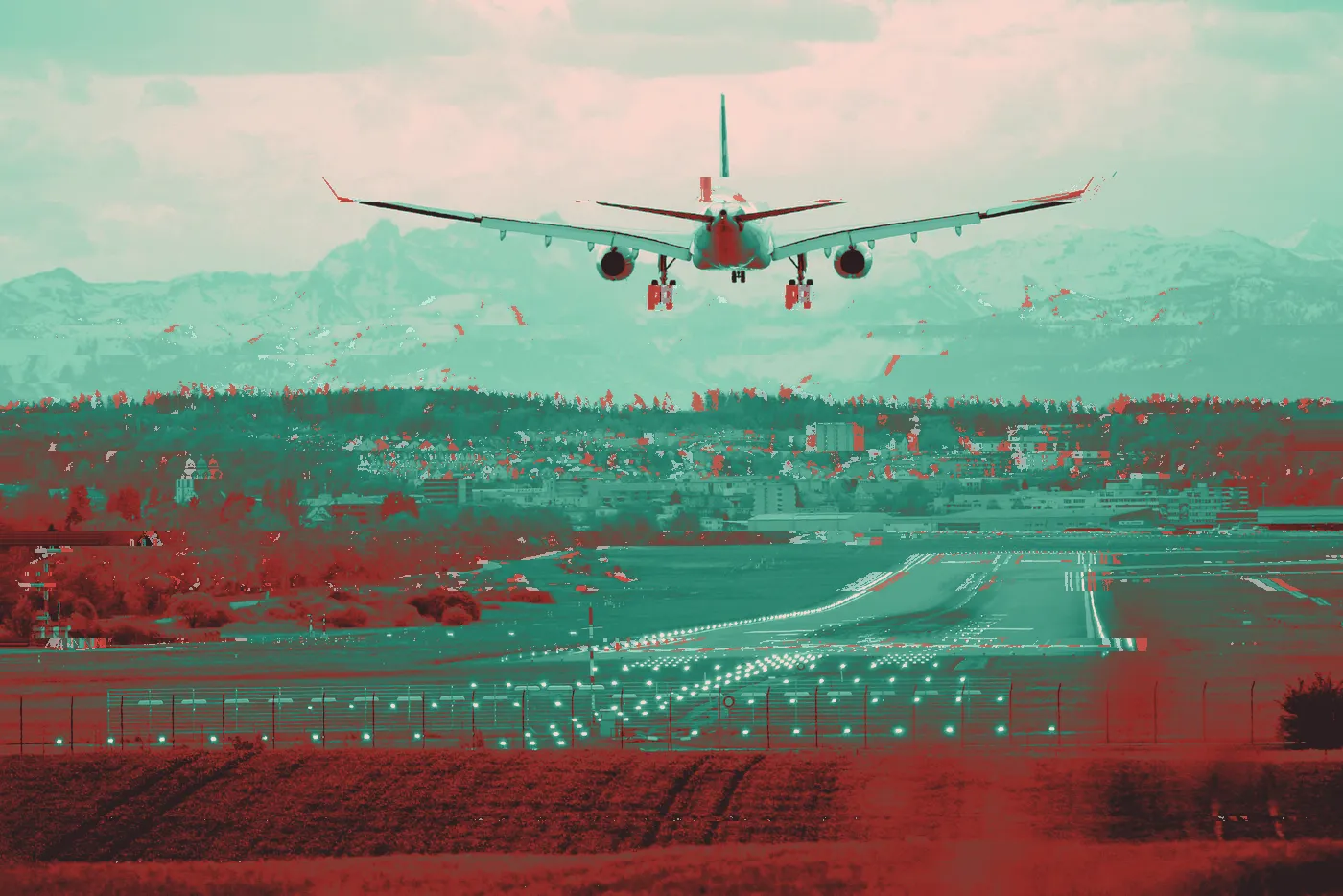Passenger jet landing toward a lit runway with snowy mountains behind