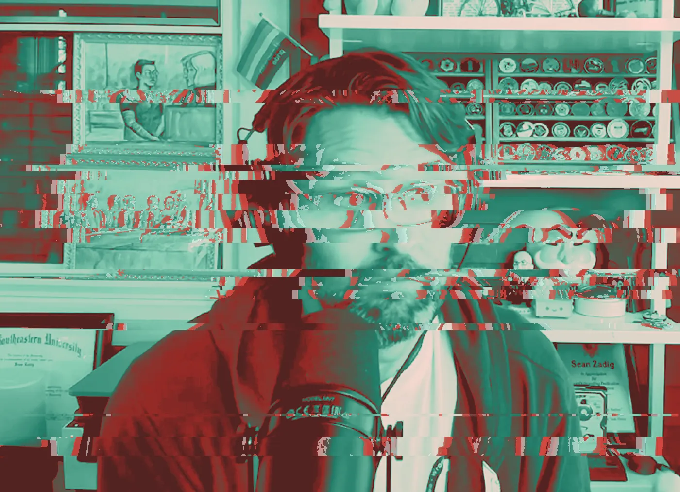 Man in headphones and purple hoodie at a podcast microphone, challenge coins on shelves behind